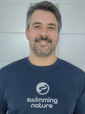Head‑and‑shoulders portrait of swimming instructor Juan Carlos in a Swimming Nature T‑shirt, smiling.