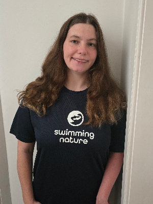 Head‑and‑shoulders portrait of swimming instructor Jennifer in a Swimming Nature T‑shirt, smiling.