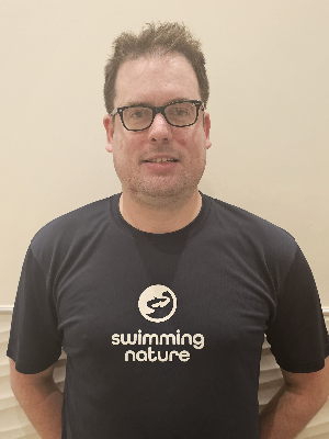 Head‑and‑shoulders portrait of swimming instructor Tom in a Swimming Nature T‑shirt, smiling.