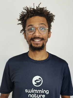 Head‑and‑shoulders portrait of swimming instructor Isham in a Swimming Nature T‑shirt, smiling.