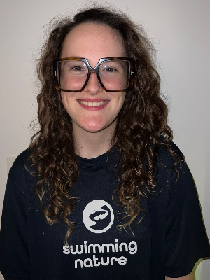 Head‑and‑shoulders portrait of swimming instructor Eden in a Swimming Nature T‑shirt, smiling.