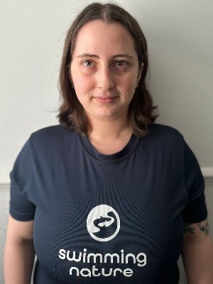 Head‑and‑shoulders portrait of swimming instructor Laura in a Swimming Nature T‑shirt, smiling.
