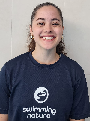 Head‑and‑shoulders portrait of swimming instructor Ella in a Swimming Nature T‑shirt, smiling.