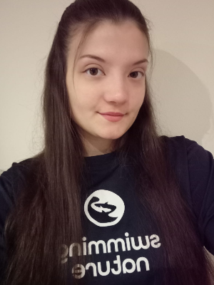 Head‑and‑shoulders portrait of swimming instructor July in a Swimming Nature T‑shirt, smiling.