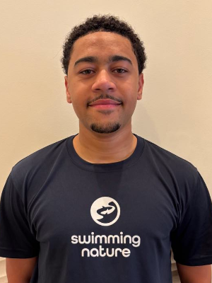 Head‑and‑shoulders portrait of swimming instructor Dylan in a Swimming Nature T‑shirt, smiling.
