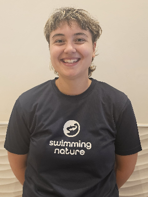 Head‑and‑shoulders portrait of swimming instructor Emma in a Swimming Nature T‑shirt, smiling.