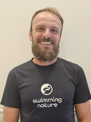 Head‑and‑shoulders portrait of swimming instructor Kris in a Swimming Nature T‑shirt, smiling.