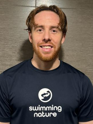 Head‑and‑shoulders portrait of swimming instructor Sam in a Swimming Nature T‑shirt, smiling.
